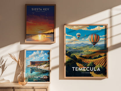 Three framed posters are displayed on a wall, featuring vibrant landscapes of Siesta Key, Dry Tortugas, and Temecula with hot air balloons over vineyards. Shadows add depth to the scene.