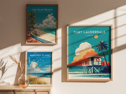 Three framed posters displaying beach scenes are hung on a sunlit wall. They feature Fort Lauderdale, Las Olas Beach, and Anastasia Island, each showcasing vibrant coastal imagery.