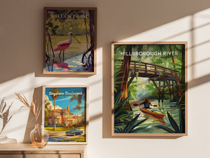 Three framed posters are displayed on a wall. The largest features a kayaker on a river under a wooden bridge, surrounded by lush greenery. Shadows and sunlight add depth.