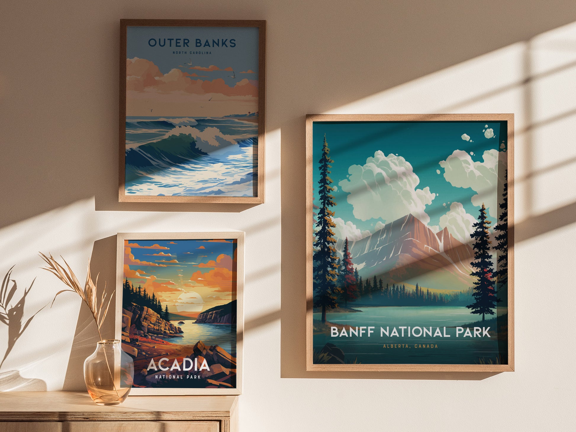 Three framed art prints are displayed on a sunlit wall, featuring landscapes of Outer Banks, Acadia National Park, and Banff National Park with vibrant colors and natural scenery.