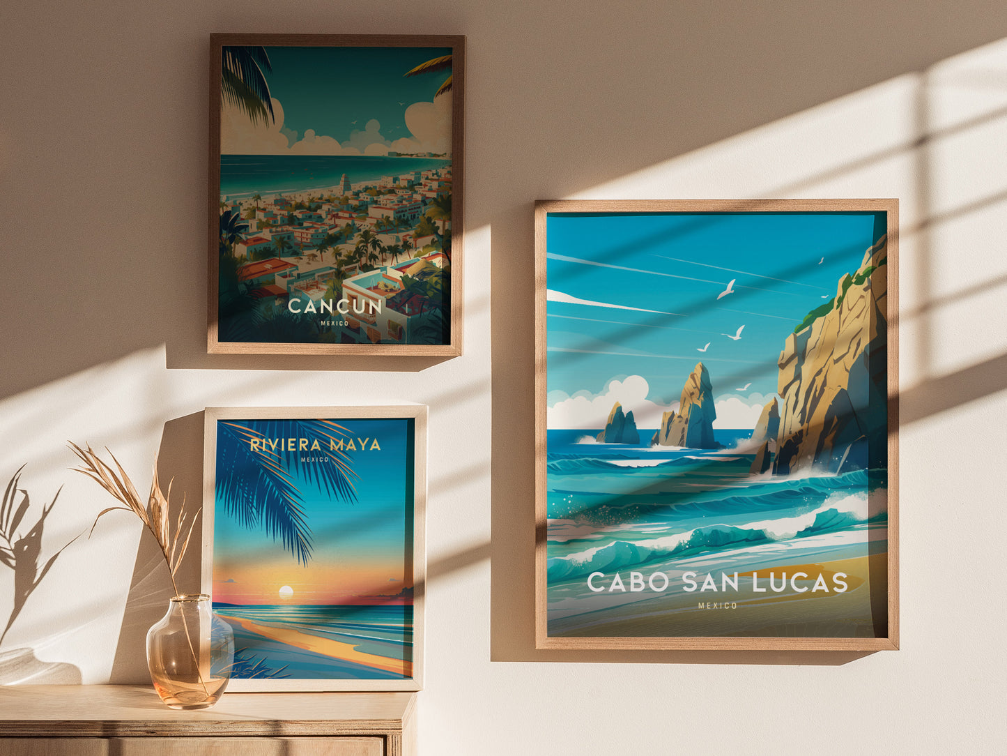 Three framed travel posters are displayed on a sunlit wall, featuring vibrant scenes of Cancun, Riviera Maya, and Cabo San Lucas, each capturing coastal landscapes and seascapes.
