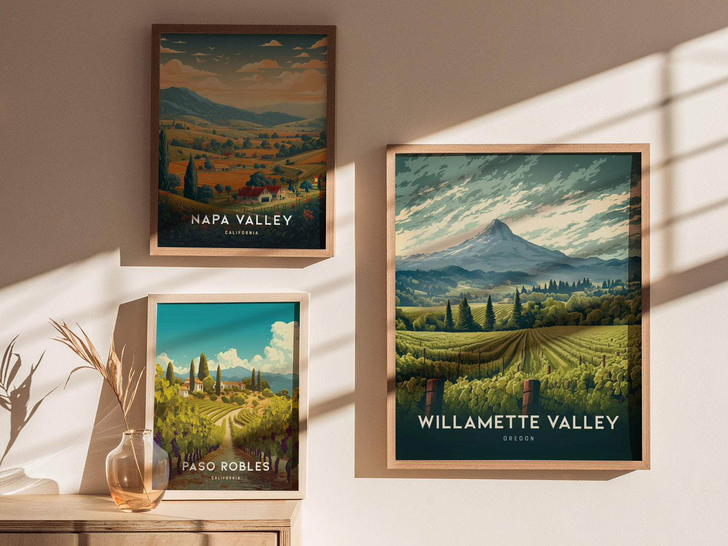 Three framed posters display scenic vineyard landscapes of Napa Valley, Willamette Valley, and Paso Robles, set against a softly lit wall with shadows and a decorative vase.