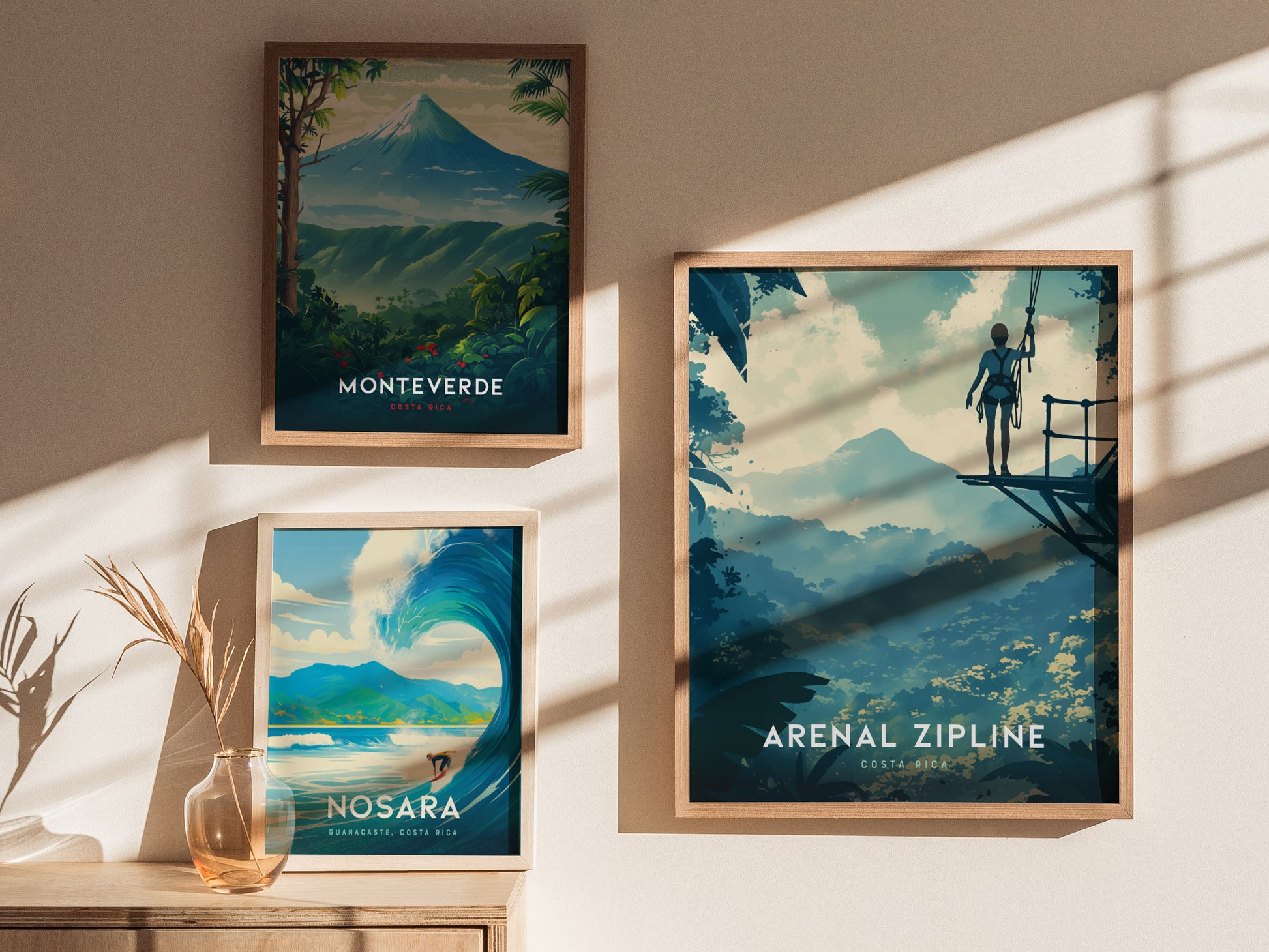Three framed travel posters are displayed on a wall, depicting scenic views of Monteverde, Nosara, and an Arenal zipline adventure in Costa Rica. Sunlight casts shadows on the wall.