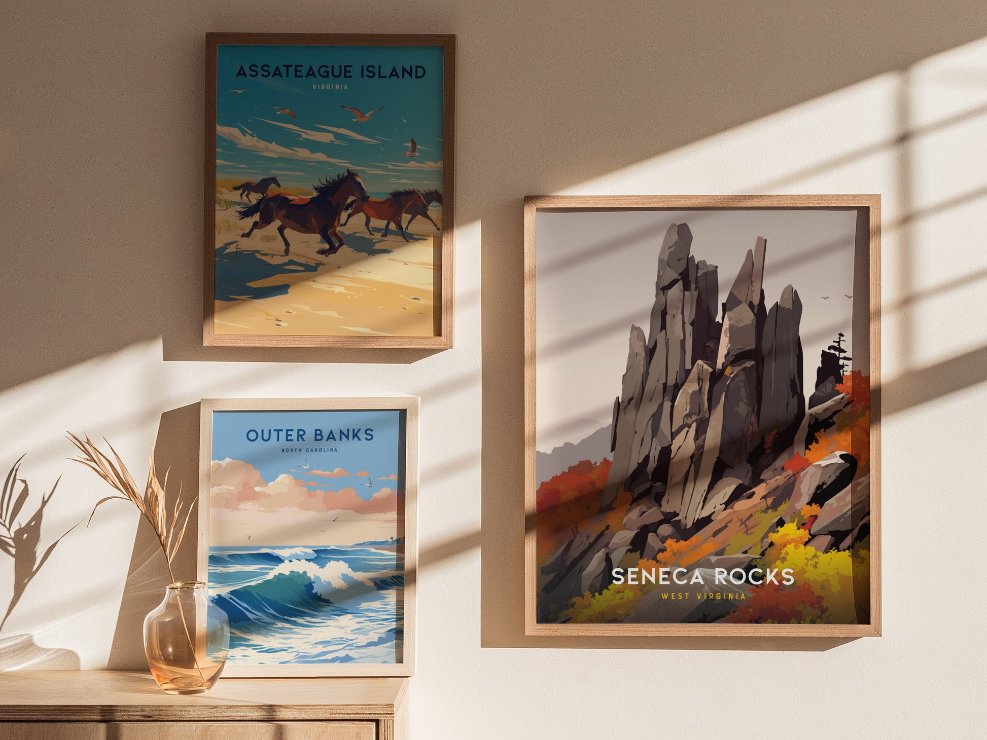 Framed artwork showcasing Seneca Rocks, Outer Banks, and Assateague Island is displayed on a sunlit wall. A vase with dried plants is on a wooden surface below.