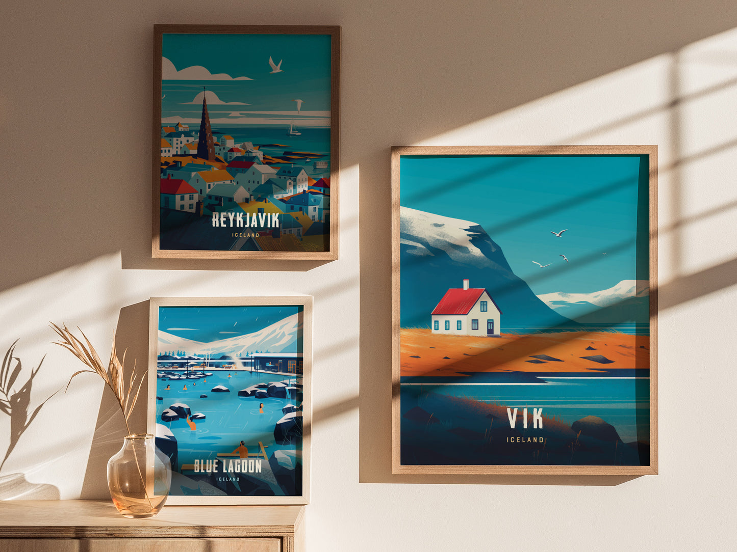 Three framed posters hang on a wall, depicting Icelandic scenes of Reykjavik, Blue Lagoon, and Vik with vibrant colors and minimalist designs. Sunlight creates shadows across the wall.