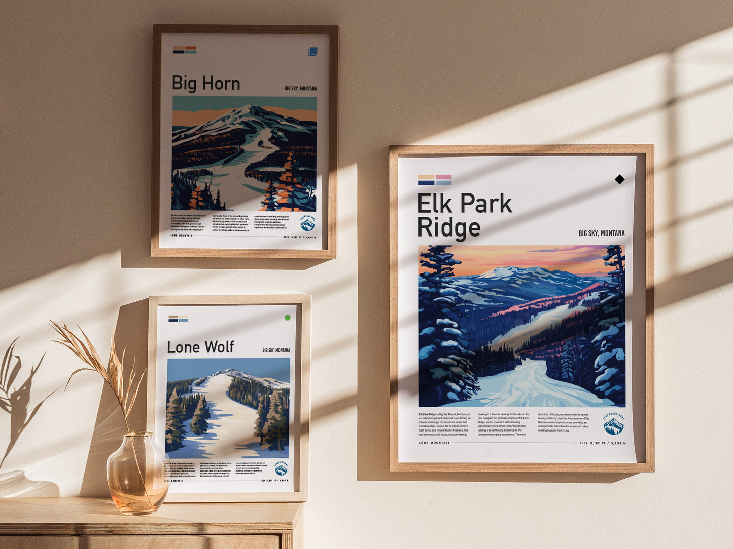 Three framed posters featuring ski runs from Big Sky, Montana are displayed on a sunlit wall. The titles are Elk Park Ridge, Big Horn, and Lone Wolf.