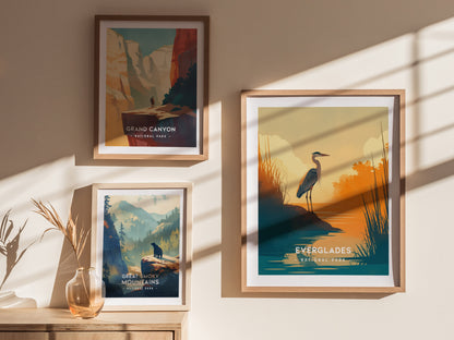 Three framed posters on a sunlit wall depict Grand Canyon, Great Smoky Mountains, and Everglades National Parks, featuring colorful landscapes and wildlife silhouettes. A vase with dried plants sits below.
