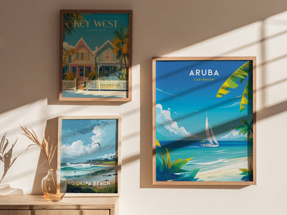 Three framed travel posters are displayed on a wall, featuring Key West, Aruba, and Hookipa Beach, each depicting vibrant coastal scenes. A vase with dried branches sits below.