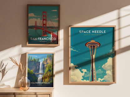 Three framed posters are displayed on a sunlit wall: the Golden Gate Bridge, Multnomah Falls, and the Space Needle in Seattle, each with vibrant colors and scenic designs.