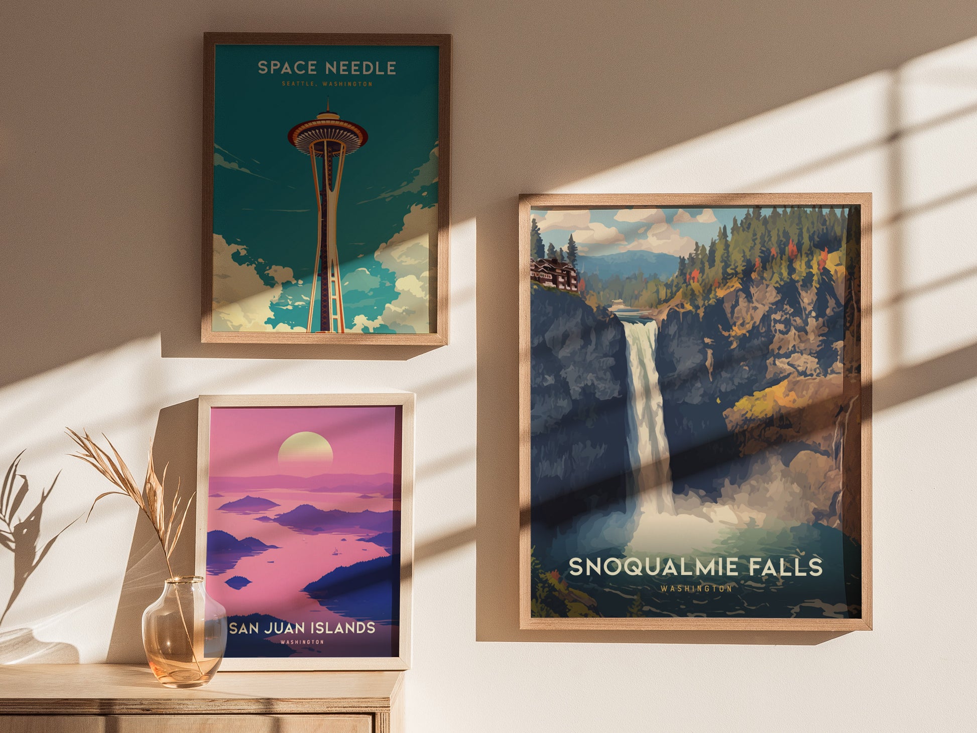 Three framed posters are displayed on a wall in warm sunlight. They depict the Space Needle, Snoqualmie Falls, and San Juan Islands, showcasing iconic Washington landmarks.