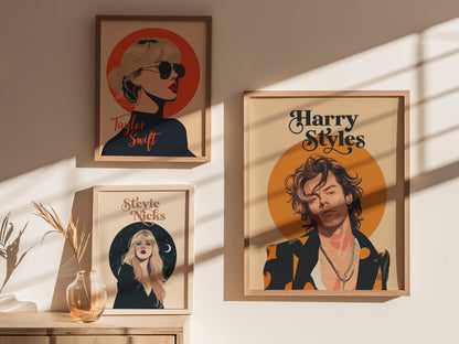 Framed posters of three pop icons, including a Harry Styles illustration with layered necklaces and orange accents, are displayed on a sunlit wall. A vase with dried plants is nearby.