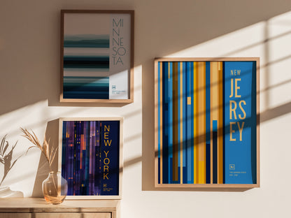 Framed posters of Minnesota, New York, and New Jersey hang on a sunlit wall, each featuring colorful vertical and horizontal lines.