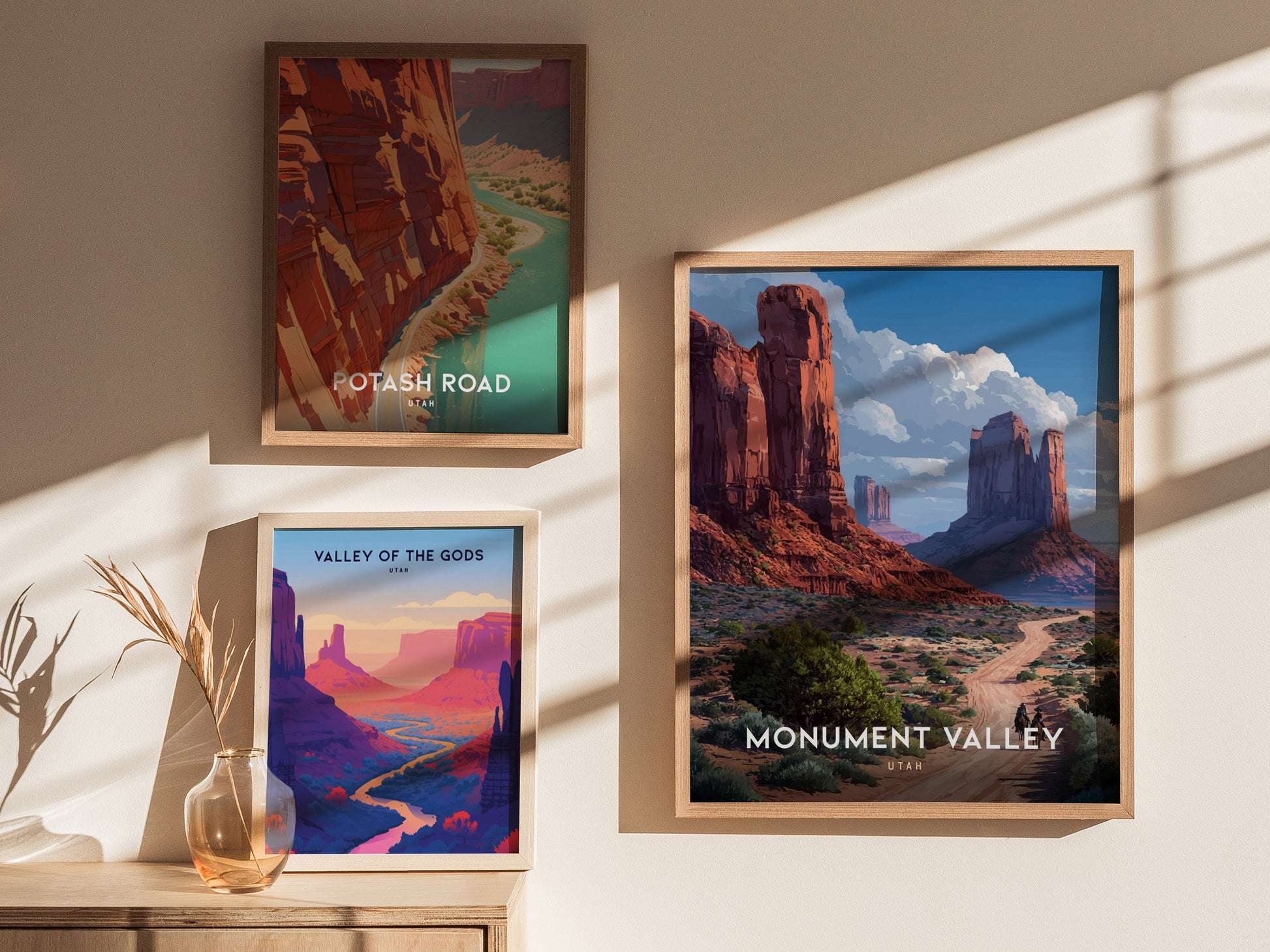 Three framed posters are displayed on a wall, showcasing Monument Valley, Potash Road, and Valley of the Gods with vivid desert landscapes. Sunlight casts shadows on the wall.