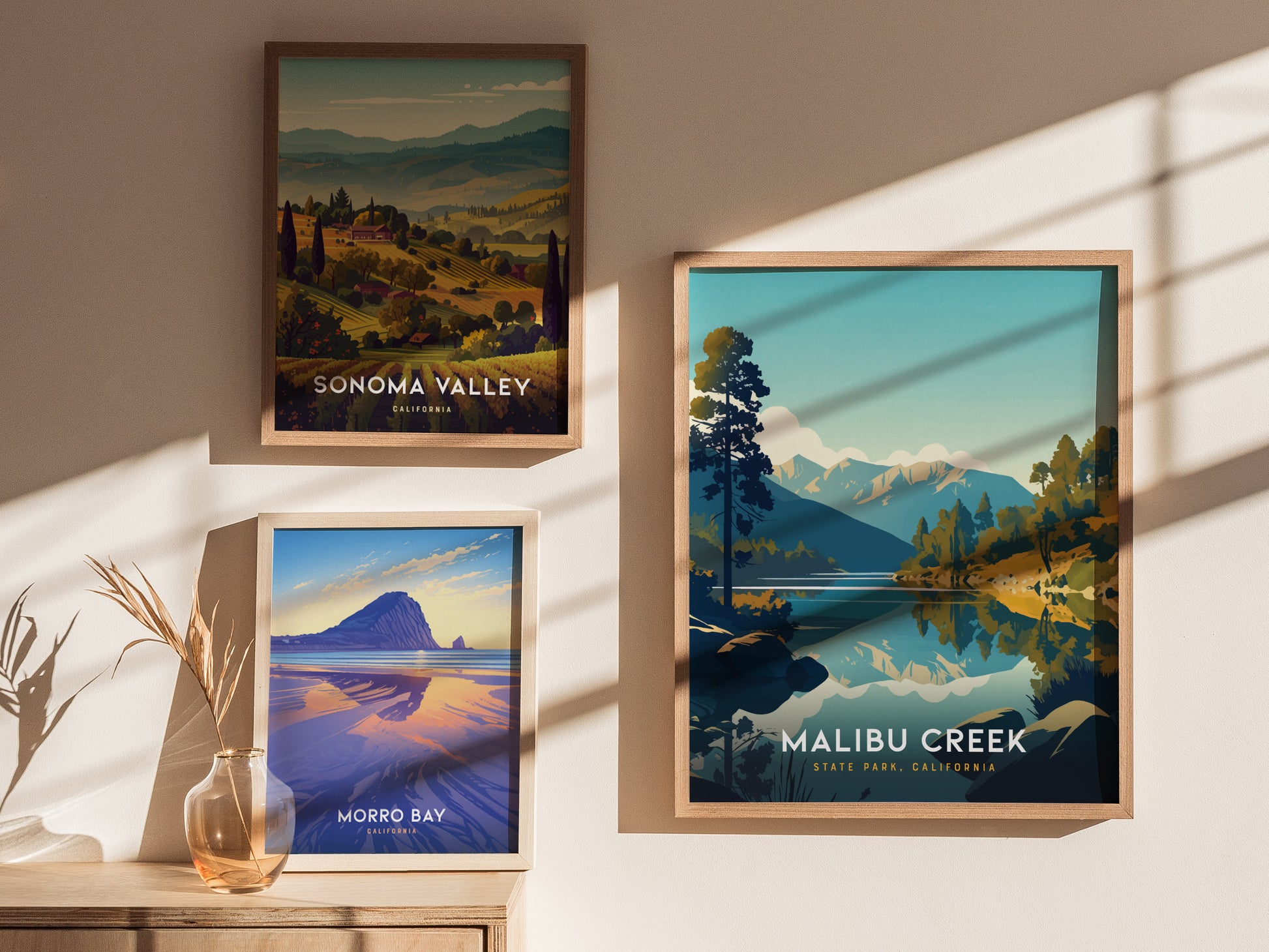 Three framed posters are displayed on a sunlit wall, featuring scenic landscapes of Sonoma Valley, Morro Bay, and Malibu Creek State Park with vibrant colors and natural beauty.