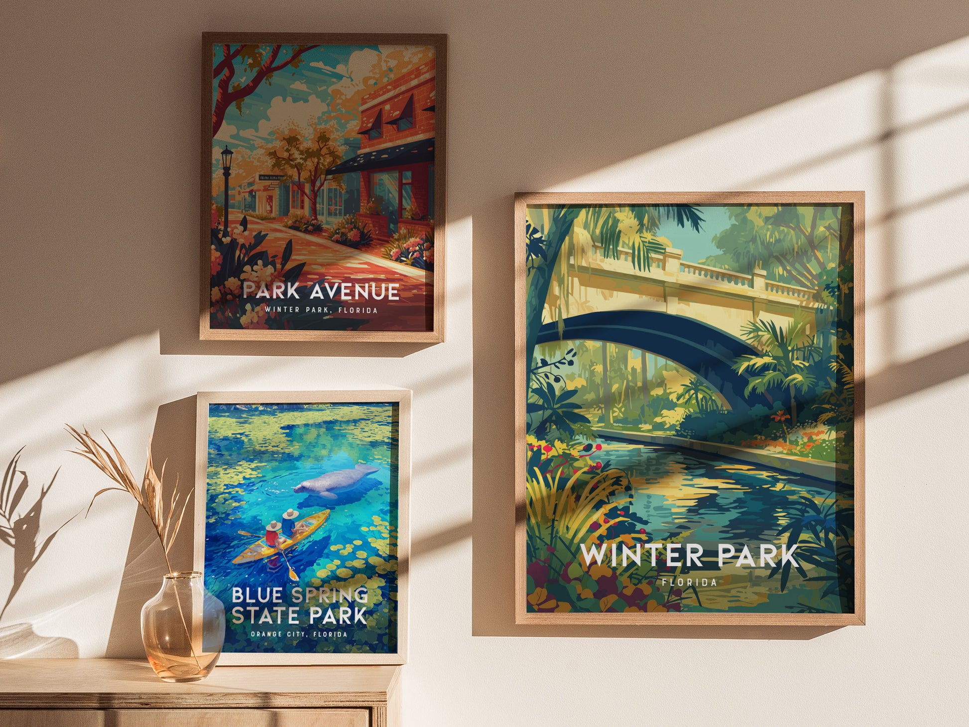 Three framed posters hang on a sunlit wall, featuring scenes from Winter Park, Florida, and Blue Spring State Park. A vase with dried plants sits on a wooden surface.