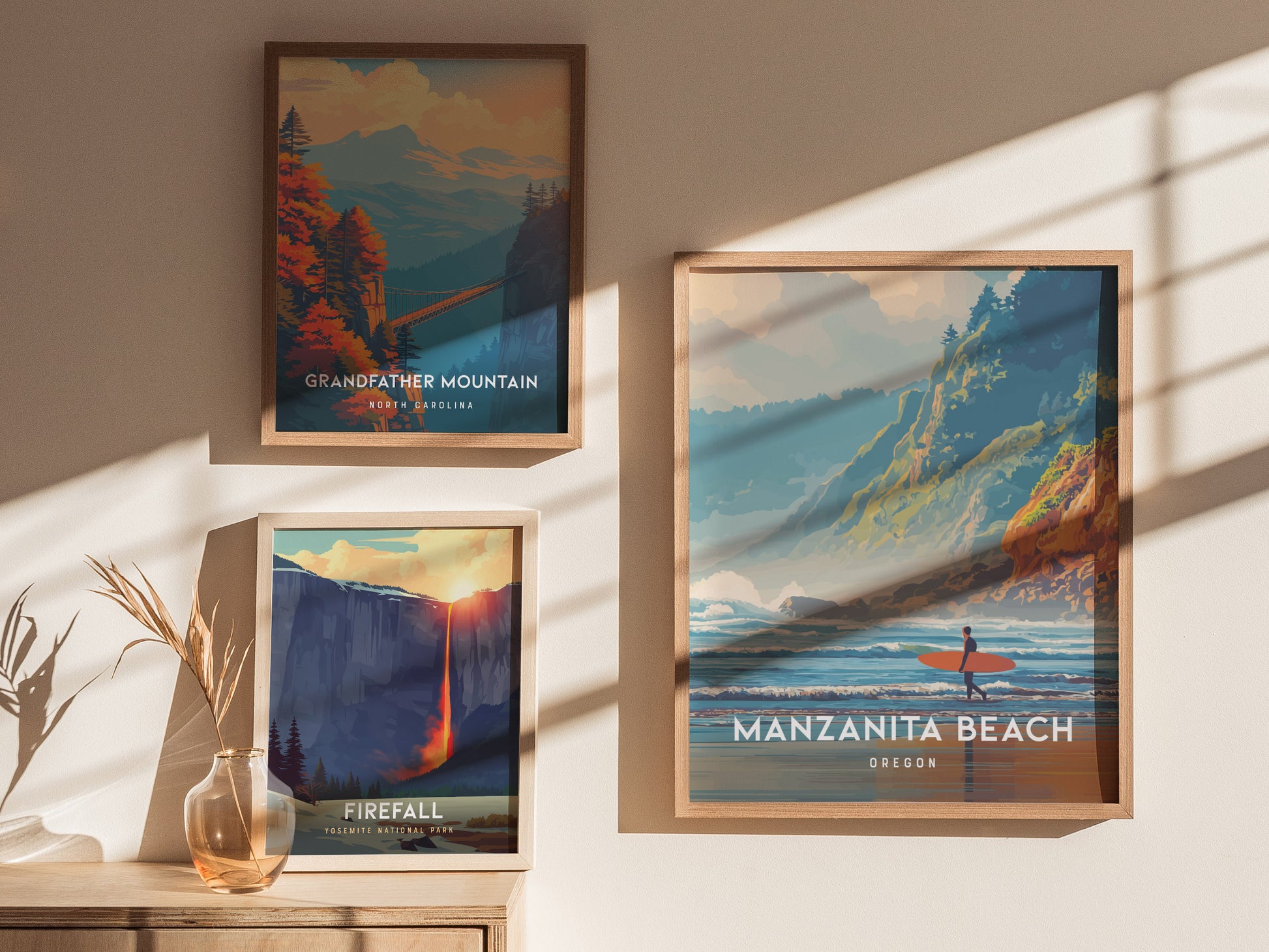 Three framed posters are displayed on a wall, featuring scenic illustrations. The central poster showcases Manzanita Beach, Oregon, with a surfer near the shore, while the others depict Grandfather Mountain and a waterfall titled Firefall.