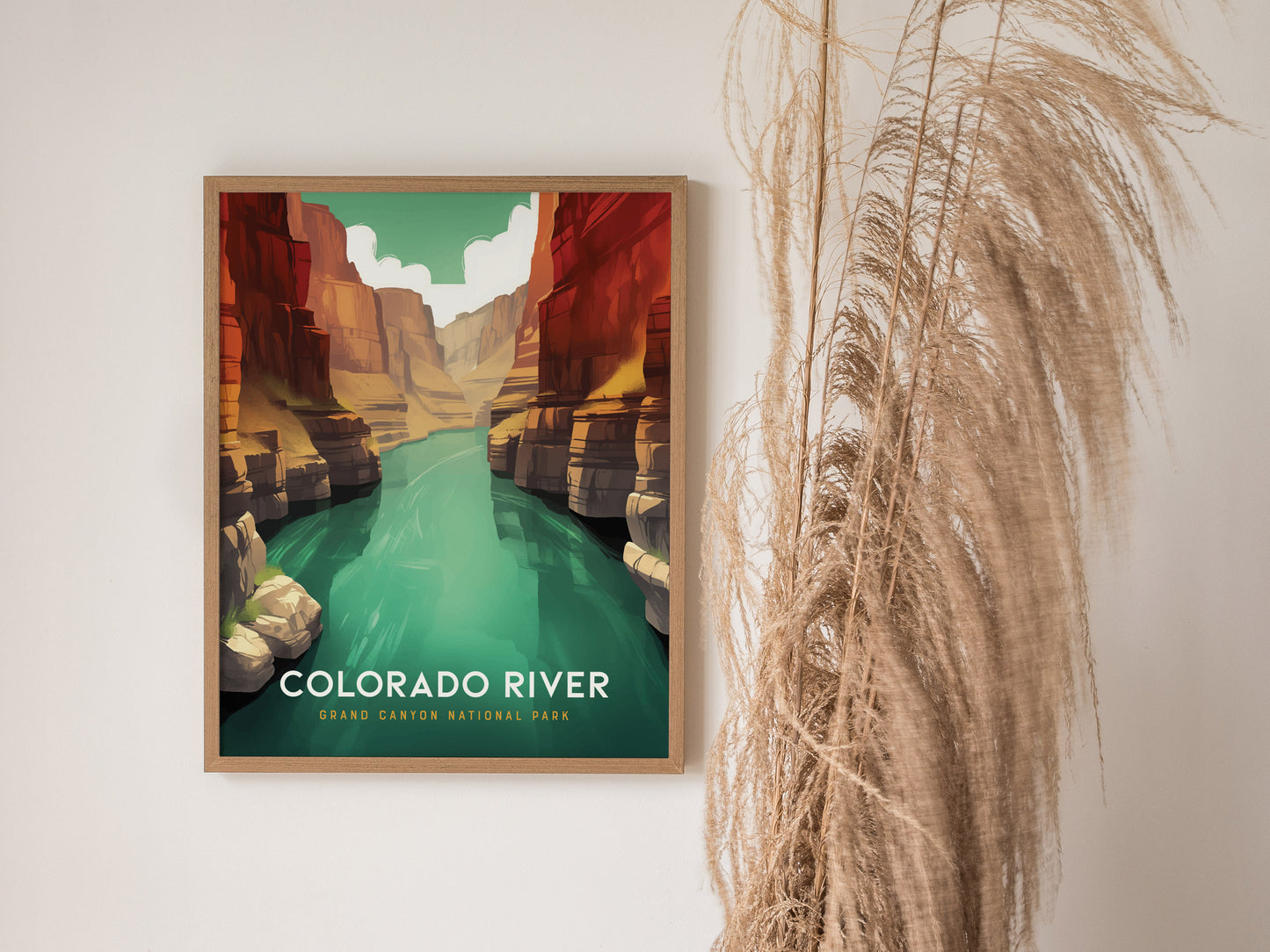 A framed poster of the Colorado River in the Grand Canyon features vivid turquoise water and rugged canyon walls, with pampas grass decoratively placed beside it.