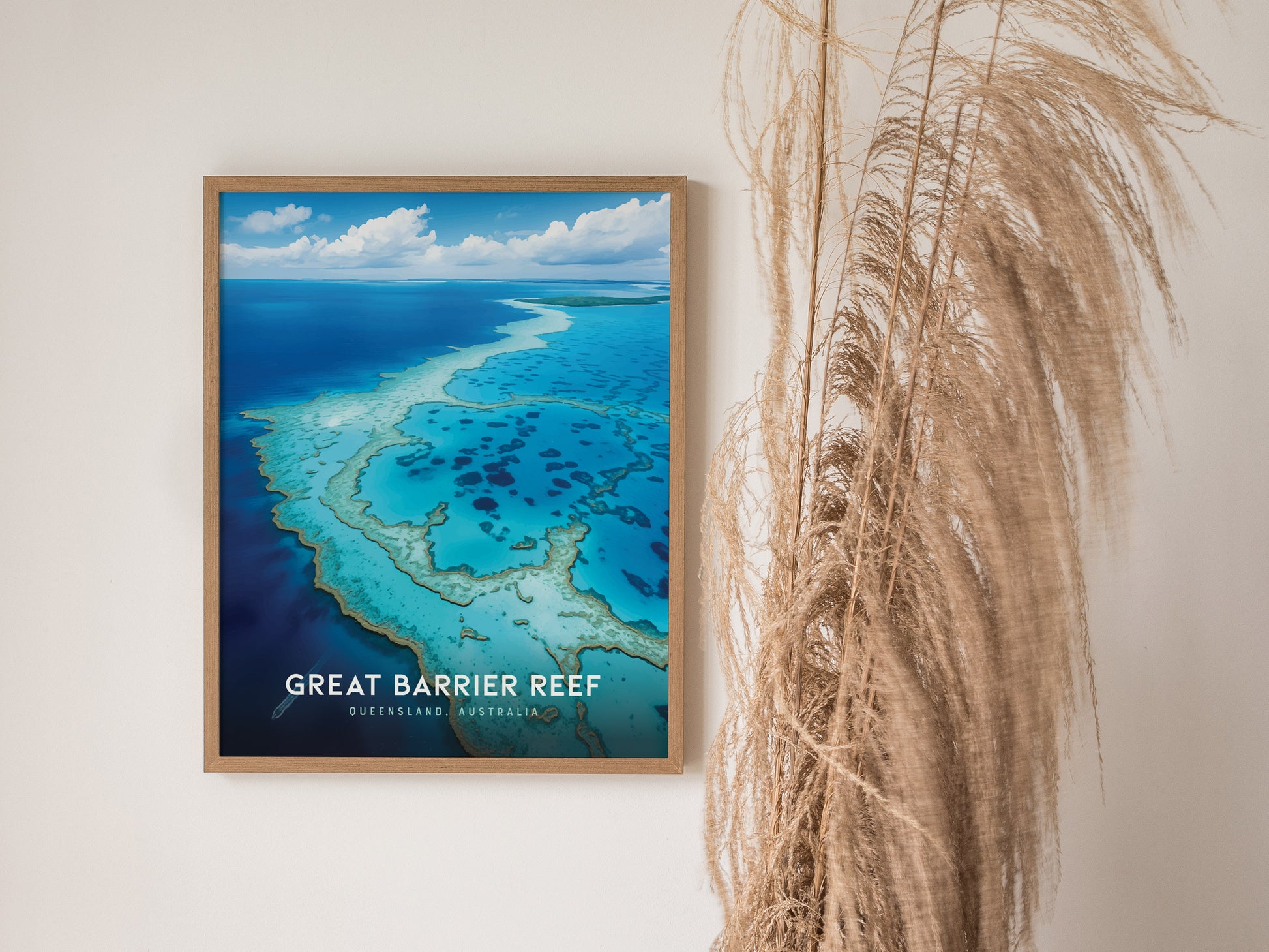 A framed poster of the Great Barrier Reef hangs on a white wall, featuring vivid turquoise waters and coral formations. Pampas grass decorates the right side, adding texture.