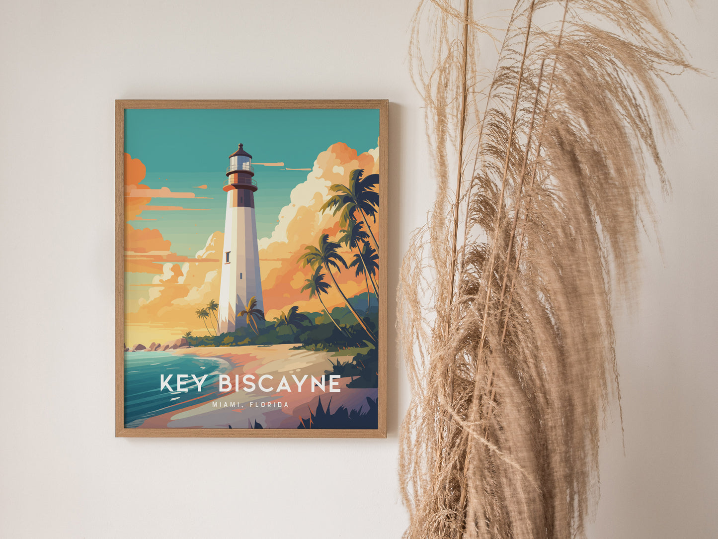 Framed Key Biscayne lighthouse poster on a wall, featuring vibrant colors of a sunset sky and swaying palm trees. Pampas grass decor is visible beside the artwork.