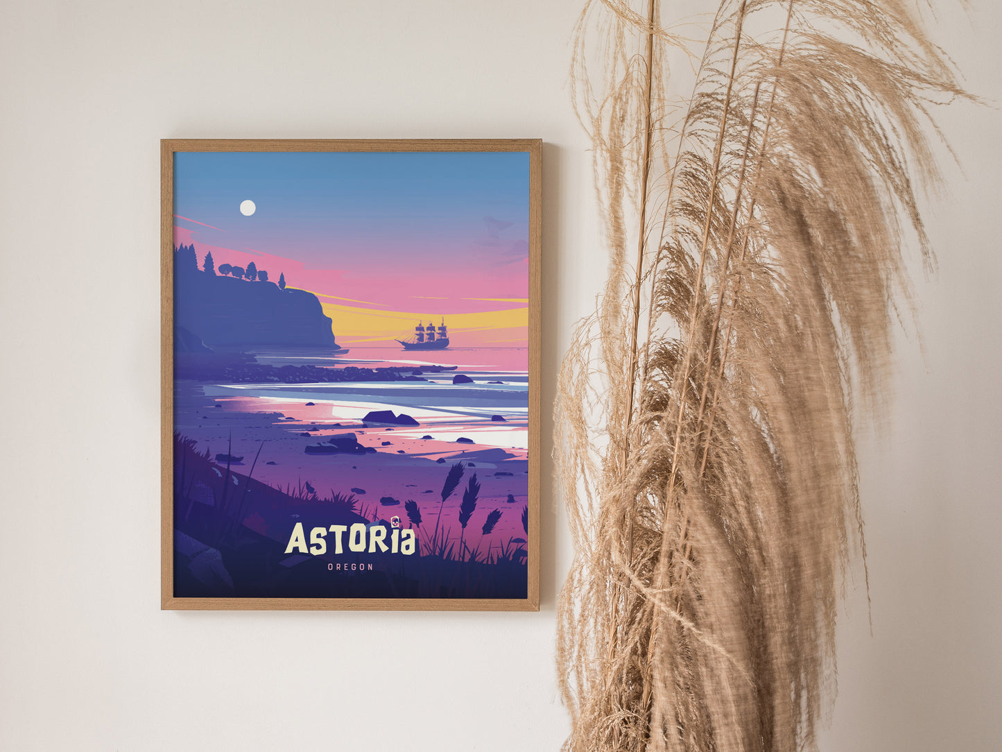 Framed poster of Astoria, Oregon, featuring a colorful sunset over the ocean with a pirate ship in the distance, displayed next to tall pampas grass.