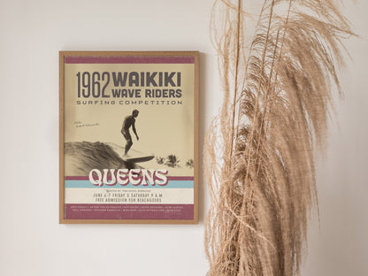A framed vintage poster for the 1962 Waikiki Wave Riders surfing competition hangs beside dry pampas grass. The design features retro typography and a surfer riding a wave.