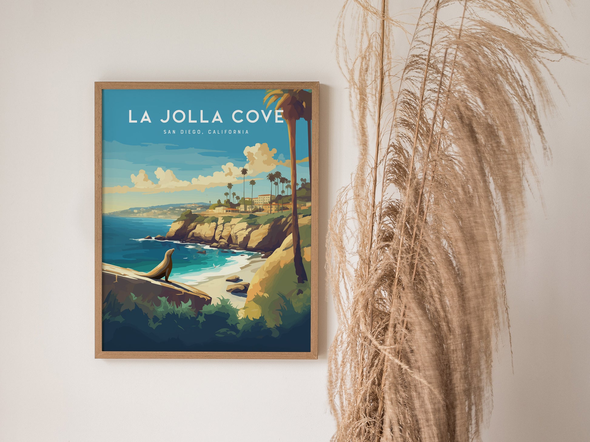A framed poster of La Jolla Cove features a vibrant coastal scene with cliffs, palm trees, and a sea lion, set against a bright blue sky.