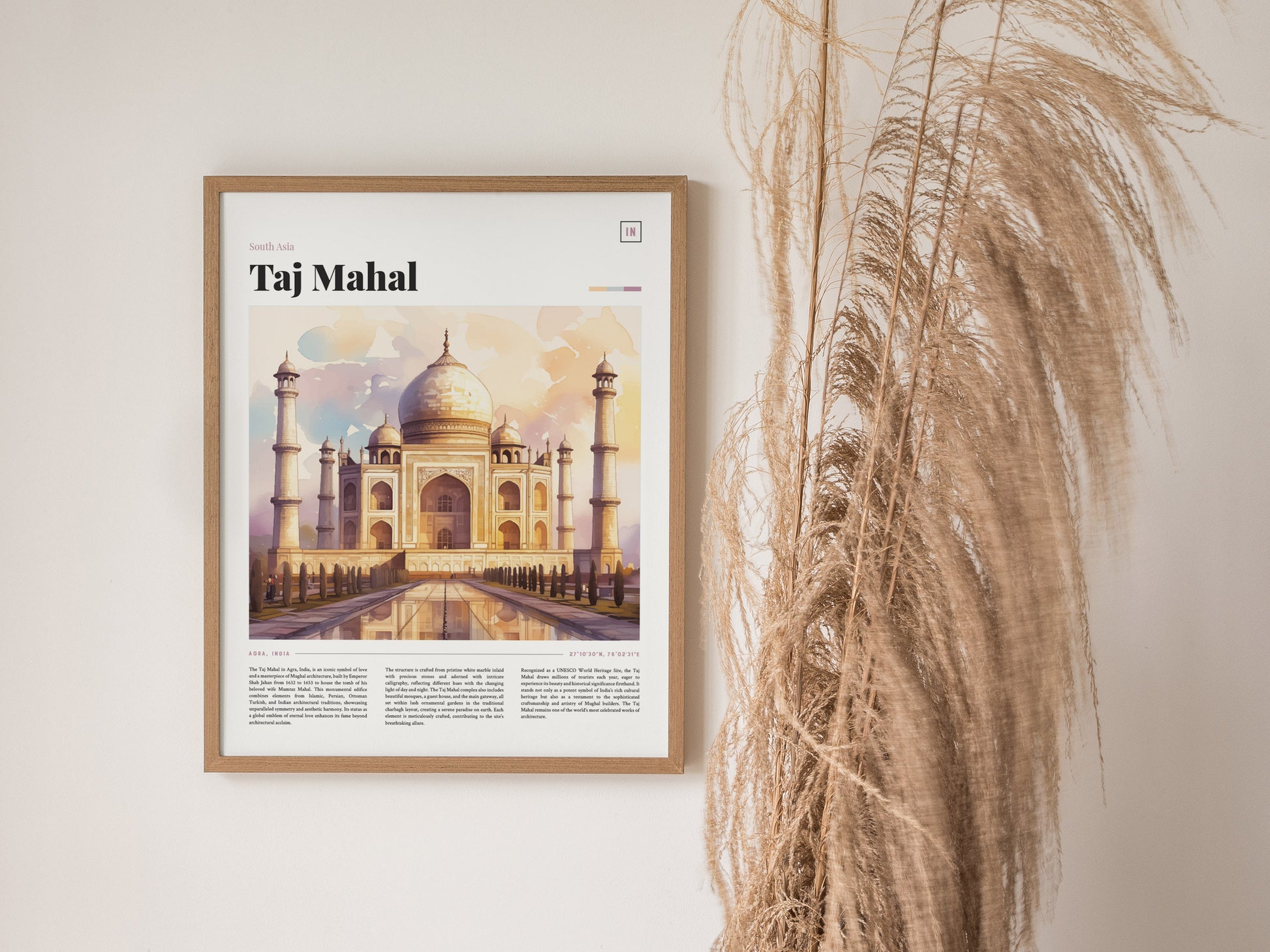 A framed poster of the Taj Mahal featuring a watercolor illustration hangs on a wall next to tall, dried grasses. The artwork highlights the monuments iconic architecture and symmetry.
