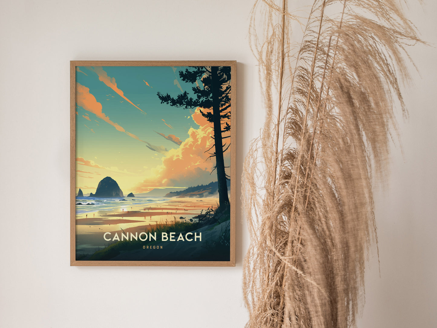 A framed poster of Cannon Beach, Oregon, featuring Haystack Rock against a vibrant sunset sky, hangs on a wall next to decorative pampas grass.