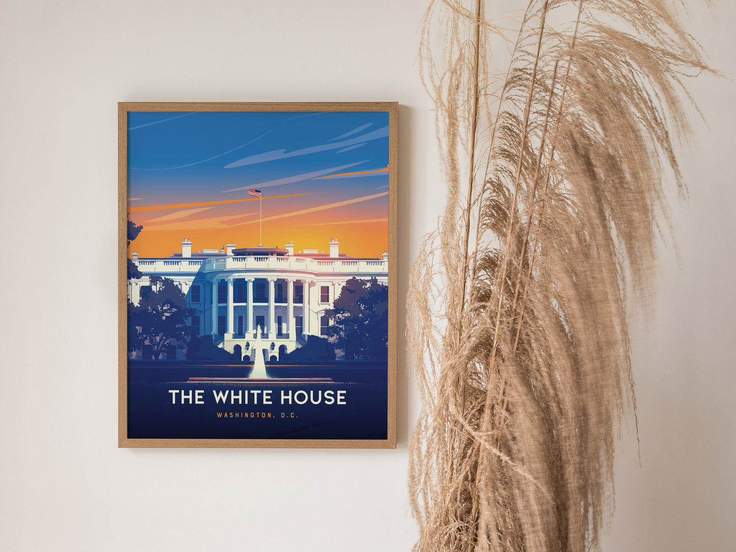 A framed poster of the White House with a vibrant sunset background hangs on a wall next to decorative pampas grass.