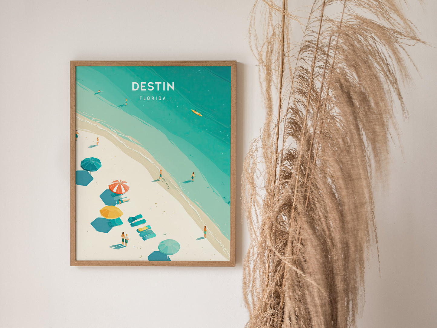 A framed poster of Destin, Florida, displaying a beach scene with turquoise waters, colorful umbrellas, and beachgoers. Dried pampas grass decorates the adjacent wall space.