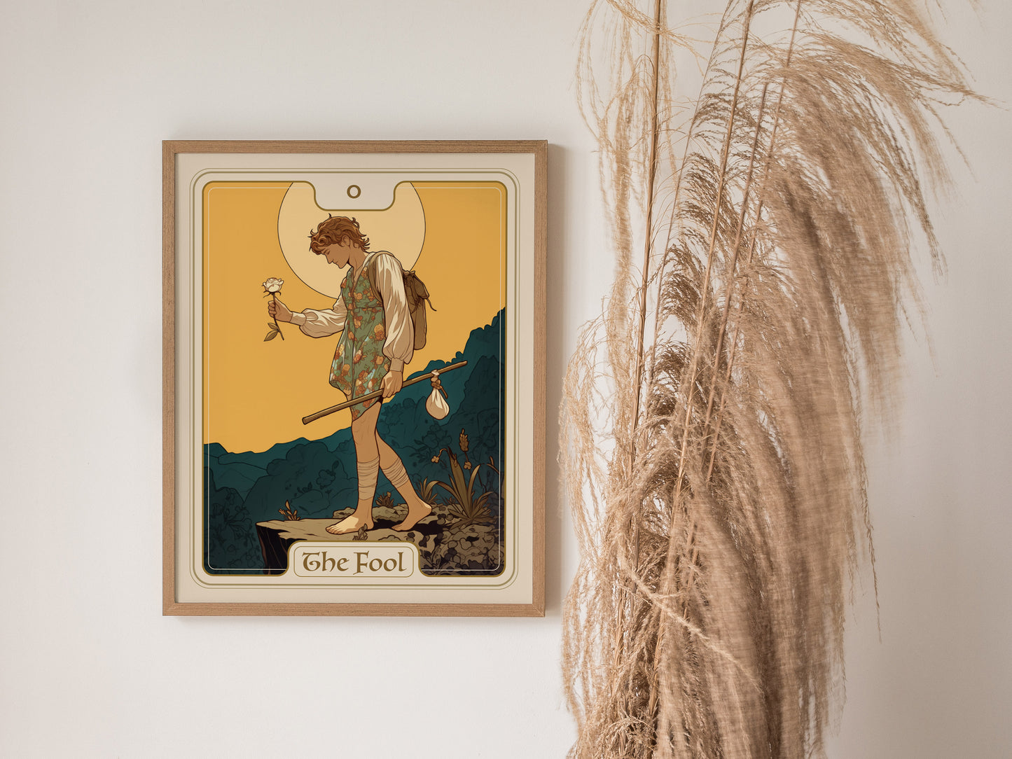 A framed tarot poster of The Fool card depicts a wanderer with a white rose and stick, set against a warm background, beside decorative dried grasses.