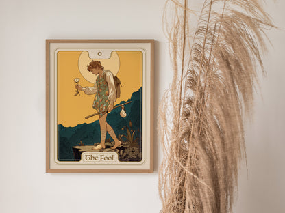 A framed tarot poster of The Fool card depicts a wanderer with a white rose and stick, set against a warm background, beside decorative dried grasses.
