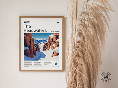 Framed poster of The Headwaters at Big Sky, Montana, depicting a snow-covered mountain landscape with rugged rocks. Tall, dried grasses stand to the right of the artwork.