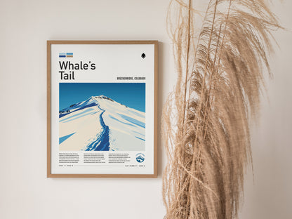 Framed Whales Tail Breckenridge poster on a white wall, featuring a minimalist depiction of a snow-covered mountain ridge. Decorative dried grasses are placed beside the poster.