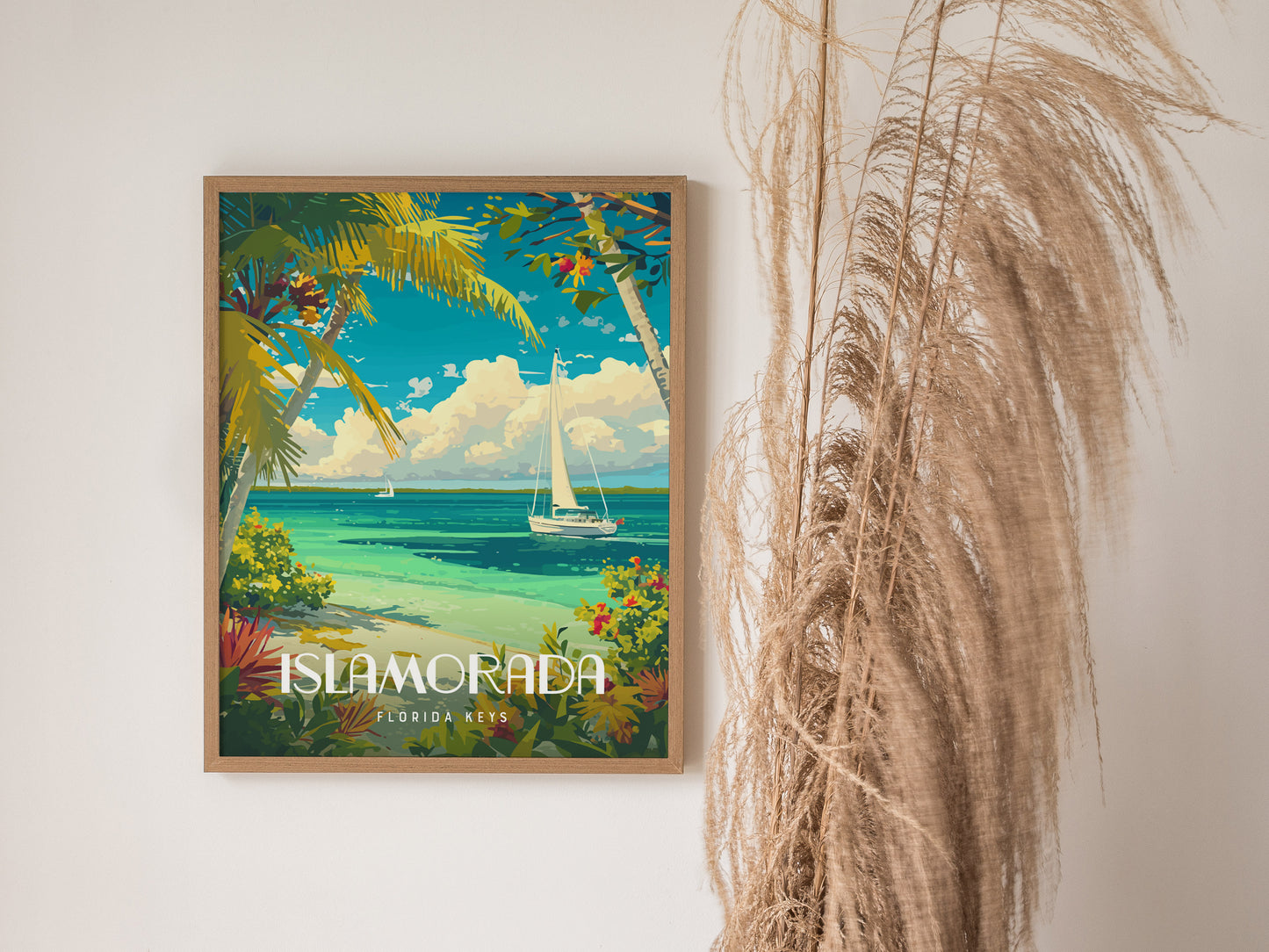 Framed Islamorada poster featuring a vibrant seascape with turquoise water, sailboats, and lush tropical foliage, displayed on a white wall beside tall dried grasses.