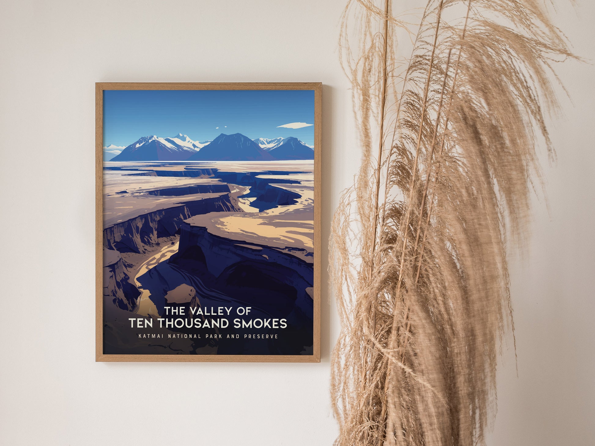 A framed poster of The Valley of Ten Thousand Smokes featuring rugged volcanic landscapes in Katmai National Park hangs on a wall beside decorative dried grasses.