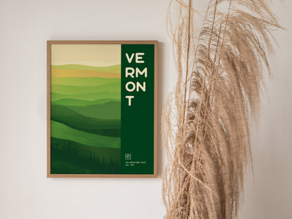 Framed poster featuring abstract green hills with VERMONT text, displayed on a wall beside dried pampas grass. The design evokes the serene landscapes of Vermont.