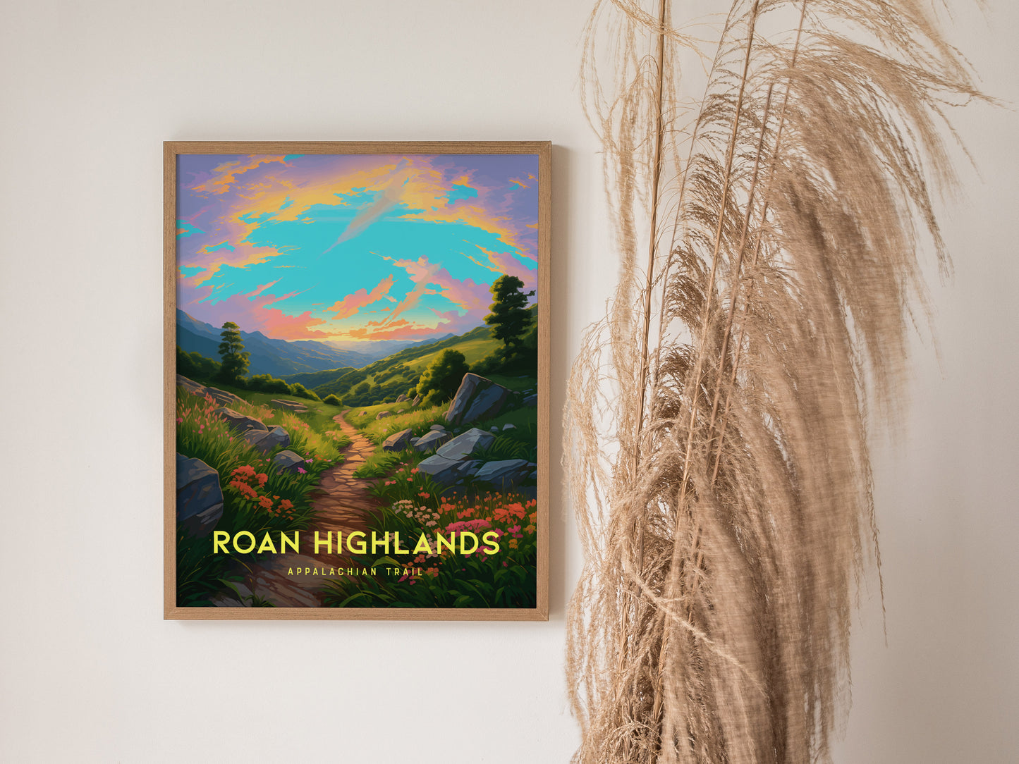 A framed poster of Roan Highlands on a wall shows a vibrant sunrise over a lush, mountainous trail. Tall, dried grasses are visible beside the artwork.