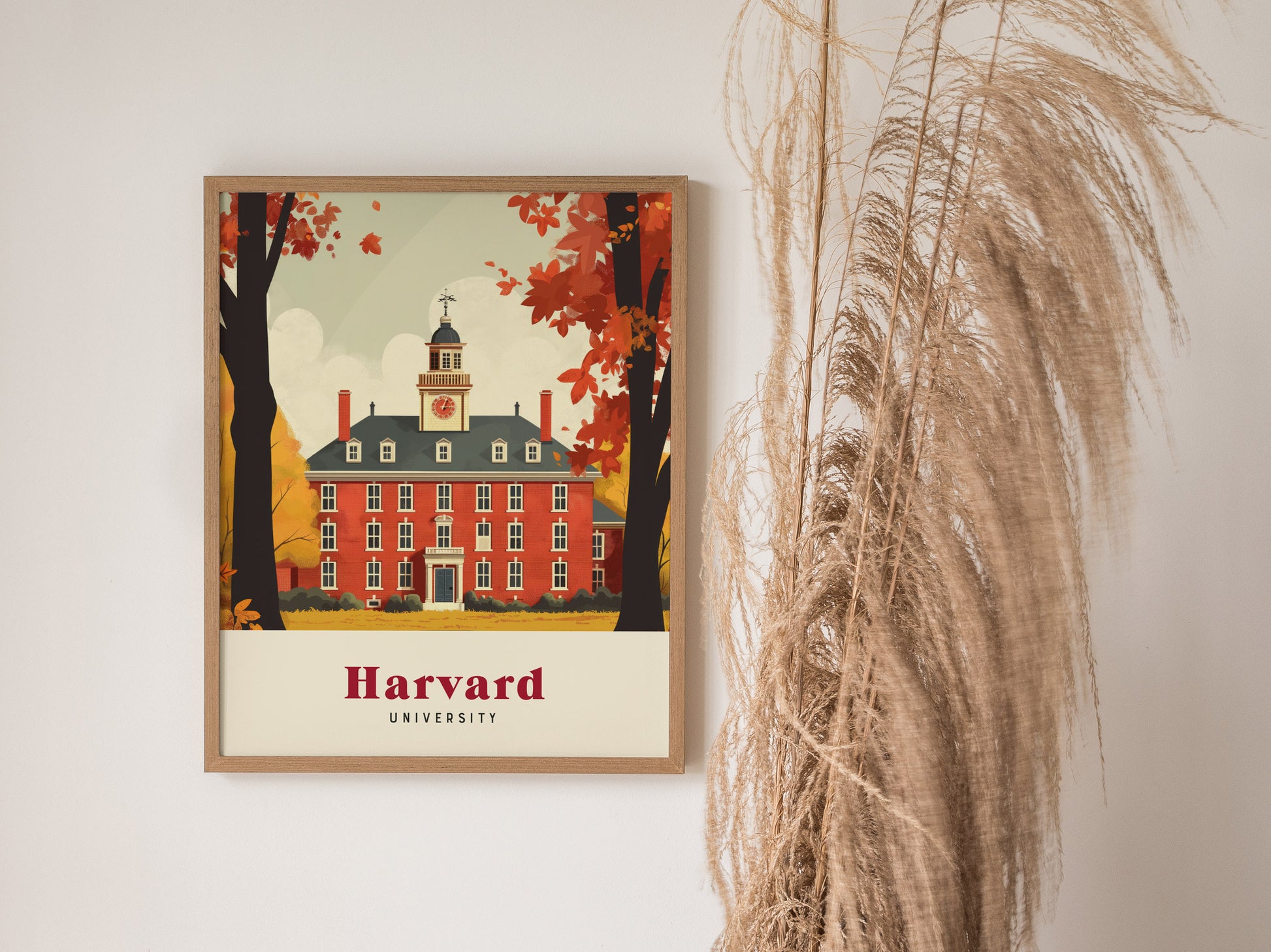 A framed poster of Harvard University features a red brick building with autumn trees, set against a light background. Tall, dried grasses are positioned to the right.
