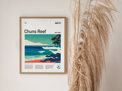 A framed poster of Chuns Reef, showcasing rolling waves and a serene beach scene under a clear sky. The artwork features vibrant colors and includes text detailing the location and surf conditions, with decorative plant elements.