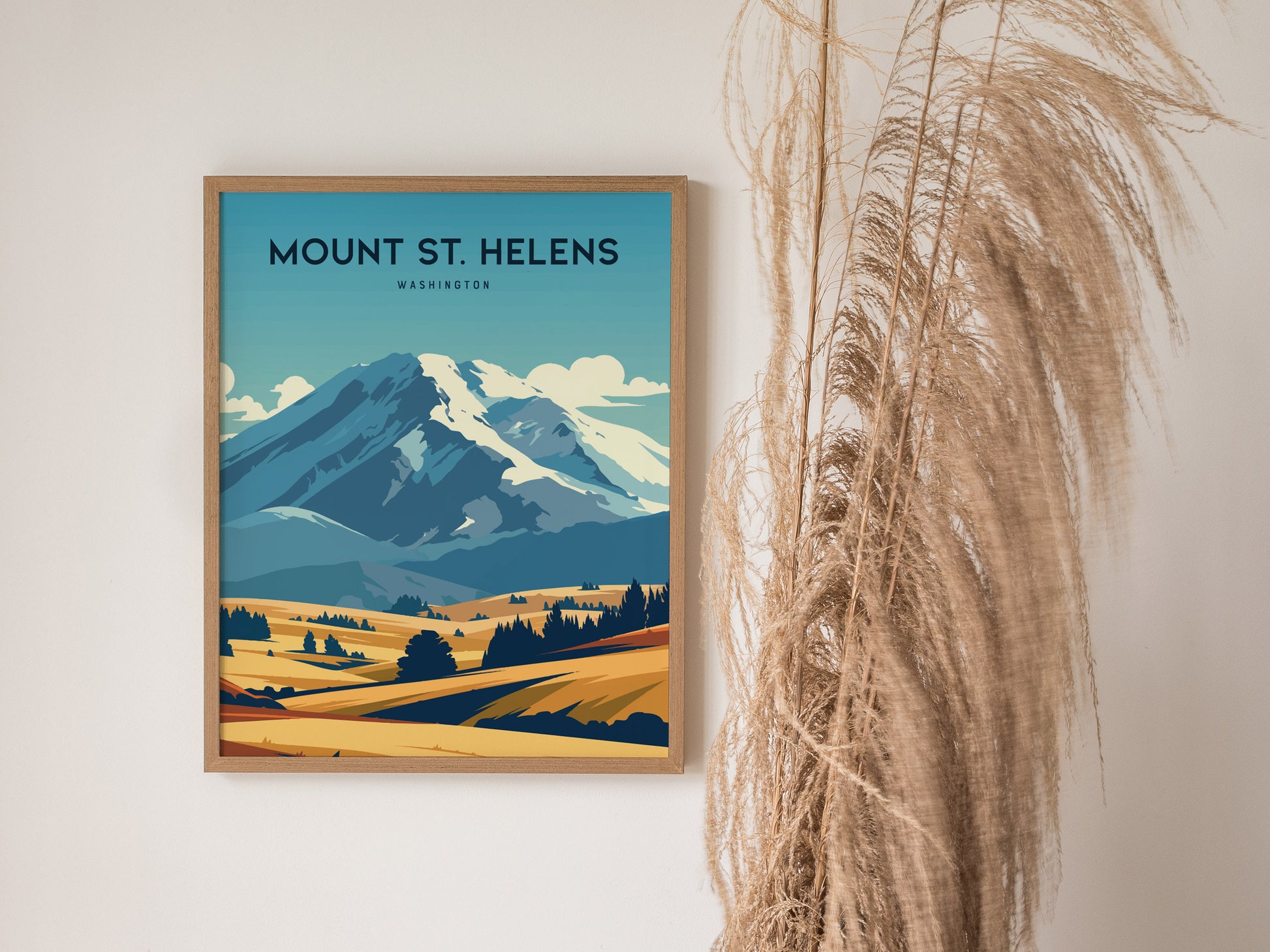 A framed Mount St. Helens poster featuring a stylized landscape with a snow-capped mountain and rolling fields, displayed beside decorative dried grass.