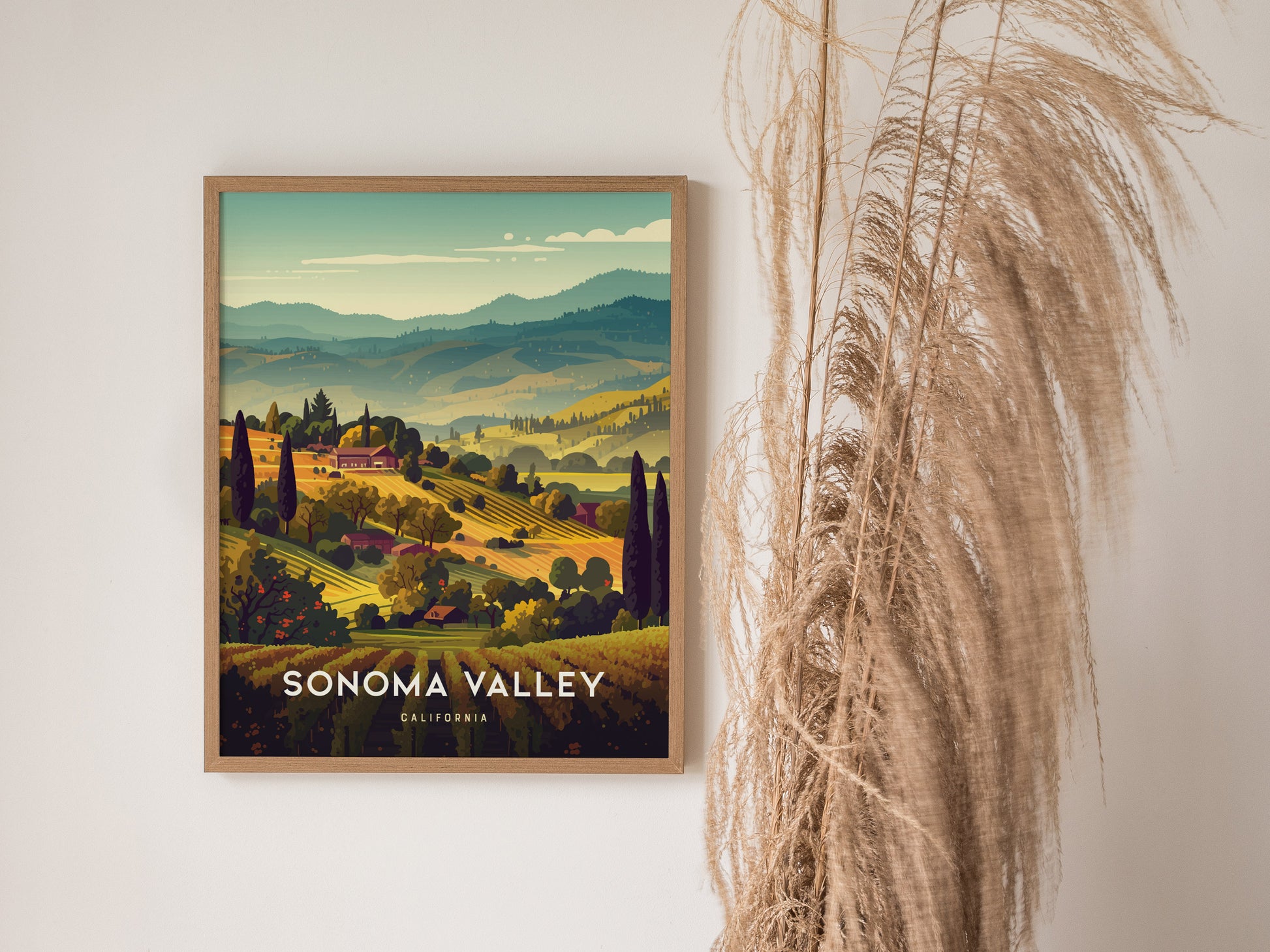 A framed Sonoma Valley poster depicting vibrant vineyard landscapes and rolling hills is displayed on a wall beside tall, wispy dried grasses.