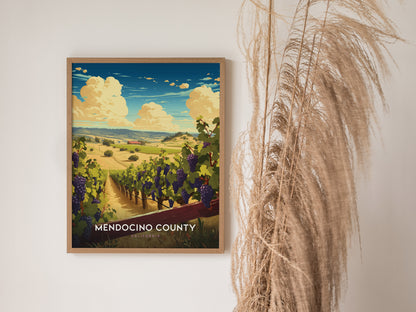 Framed artwork of Mendocino County featuring vineyards under a blue sky with fluffy clouds. The poster is displayed on a white wall next to tall, dry pampas grass.