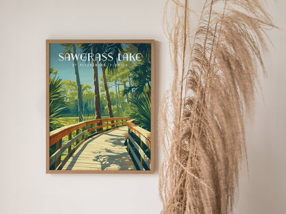 Framed poster of Sawgrass Lake Park with a wooden boardwalk surrounded by lush greenery. Decorative dried grasses are placed beside the poster against a plain white wall.