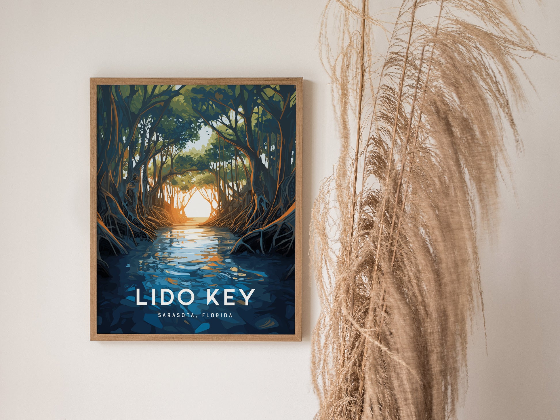 A framed poster of Lido Key Mangroves hangs on a wall, depicting sunlit water and arching mangrove canopies. Dried grasses are arranged next to it, enhancing the natural aesthetic.