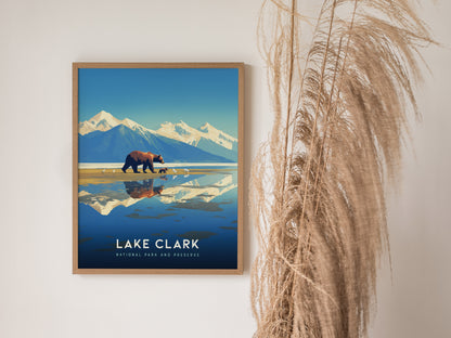 Framed artwork of Lake Clark National Park featuring a bear and cubs walking along the shore, with snow-capped mountains in the background, displayed next to tall dried grasses.