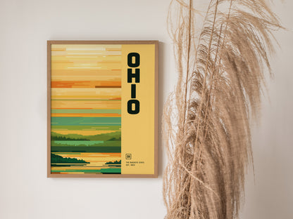 A framed poster with OHIO in bold text against a minimalist landscape design in earthy tones, displayed next to tall dried grasses.