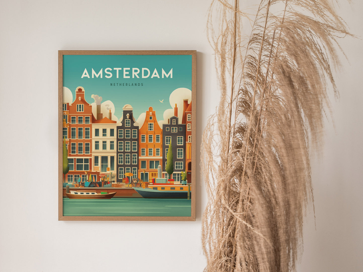 Framed artwork of Amsterdam canals featuring colorful historic buildings and boats, with a decorative dried plant beside it on a plain wall.
