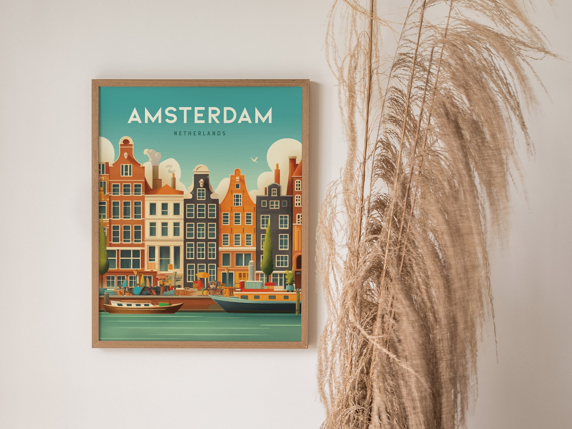 Framed artwork of Amsterdam canals featuring colorful historic buildings and boats, with a decorative dried plant beside it on a plain wall.