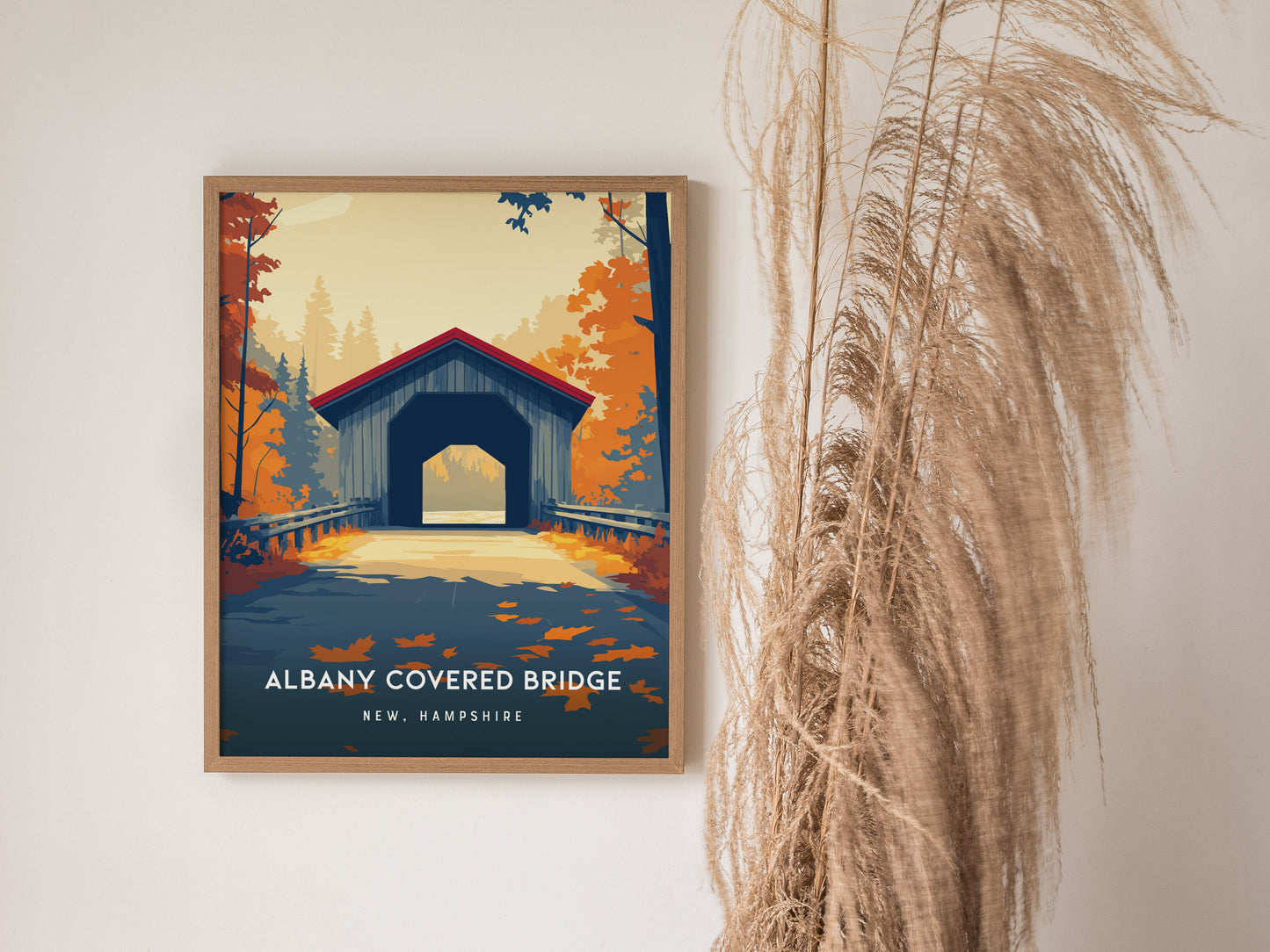 A framed poster of the Albany Covered Bridge in New Hampshire is displayed against a light wall, showcasing a vibrant illustration of the bridge surrounded by colorful autumn foliage.